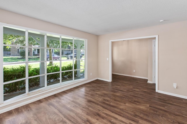 spare room featuring dark wood-style floors, a textured ceiling, and baseboards