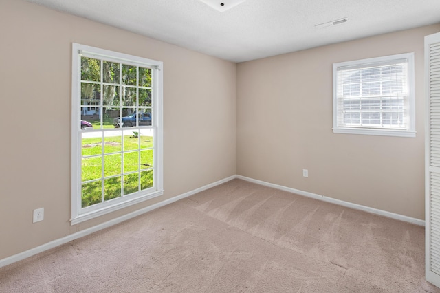 empty room featuring light carpet, a textured ceiling, visible vents, and baseboards