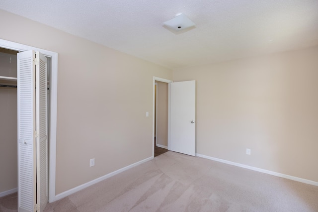 unfurnished bedroom featuring a closet, light carpet, a textured ceiling, and baseboards