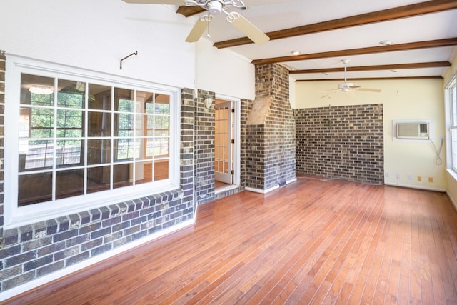 unfurnished living room with a wall unit AC, wood-type flooring, lofted ceiling with beams, ceiling fan, and brick wall