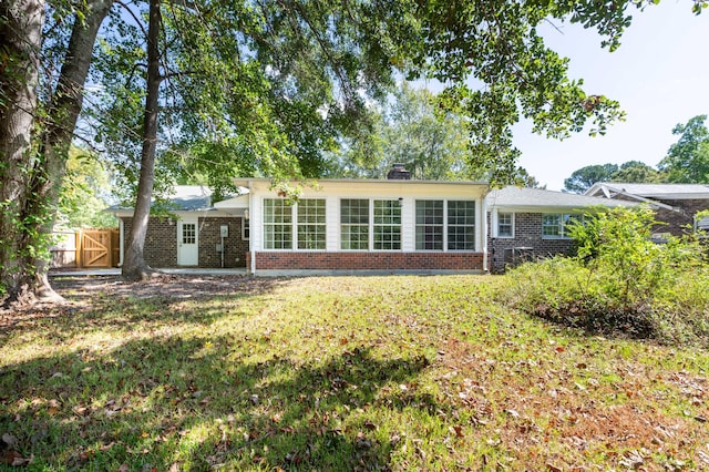 rear view of house with brick siding, a lawn, a chimney, and fence