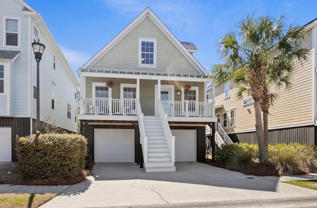 coastal inspired home featuring a porch, concrete driveway, an attached garage, and stairs