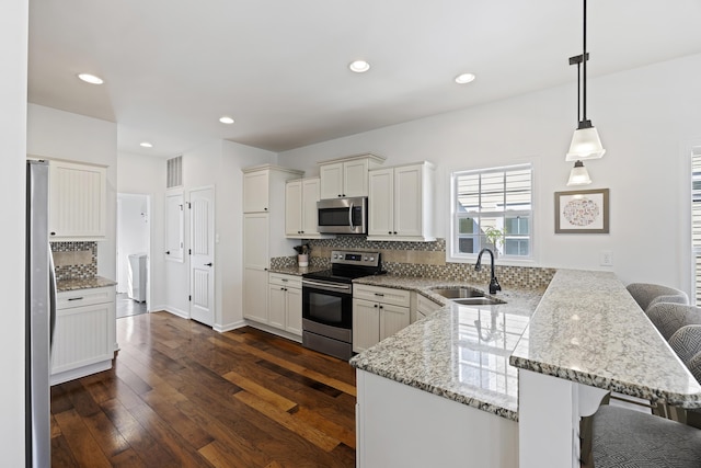 kitchen with tasteful backsplash, appliances with stainless steel finishes, dark wood-type flooring, a sink, and a peninsula