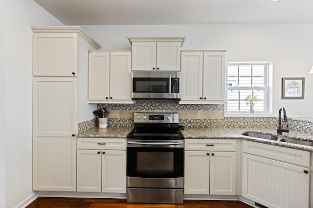 kitchen featuring appliances with stainless steel finishes, a sink, decorative backsplash, and light stone countertops