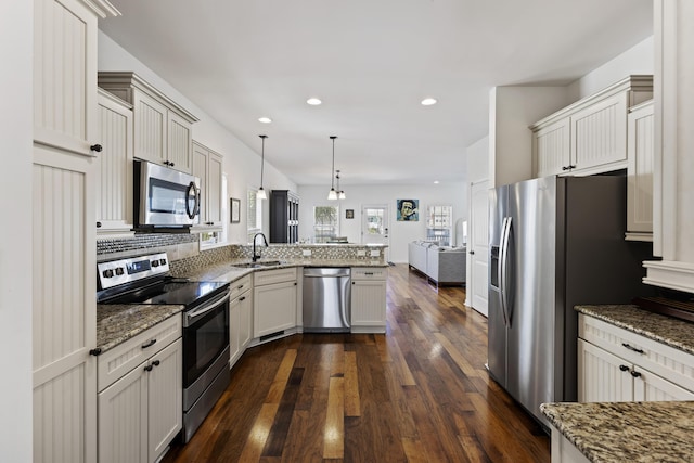 kitchen featuring open floor plan, dark wood-style flooring, a peninsula, stainless steel appliances, and a sink