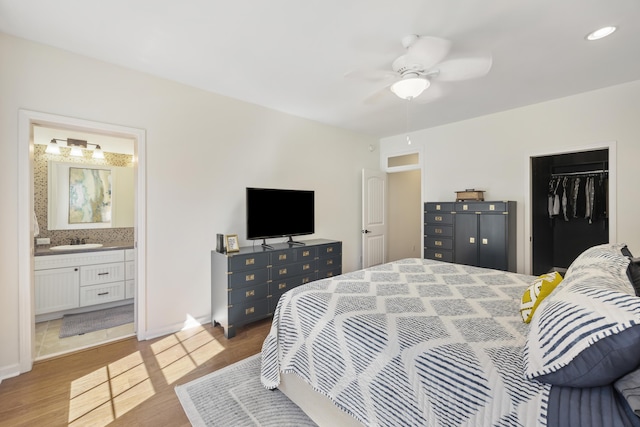 bedroom with baseboards, ensuite bathroom, a sink, and wood finished floors