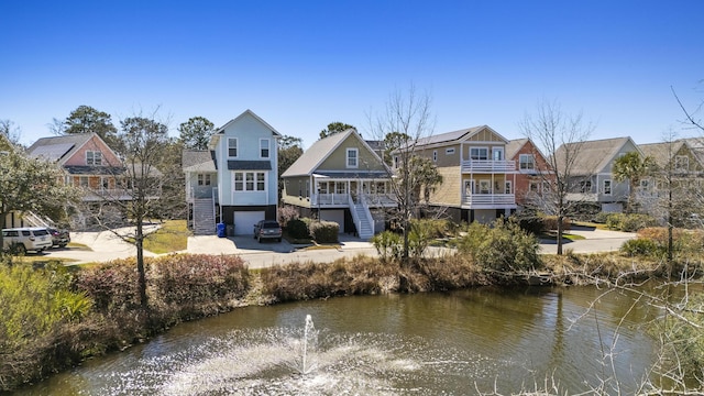 back of property with an attached garage, a water view, a residential view, and concrete driveway