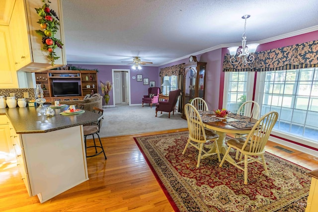 dining room with ceiling fan with notable chandelier, a textured ceiling, light wood-type flooring, and ornamental molding