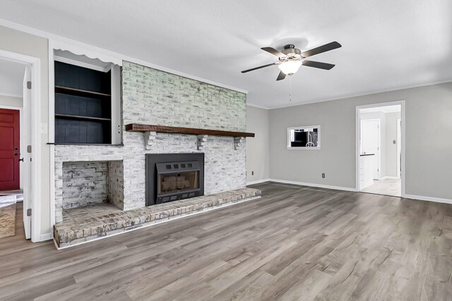 unfurnished living room featuring wood finished floors, baseboards, ceiling fan, crown molding, and a brick fireplace