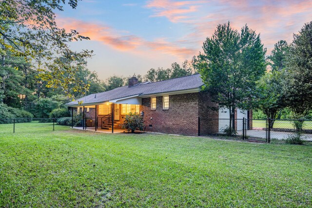 view of front of home with brick siding, a lawn, a chimney, a garage, and a fenced backyard