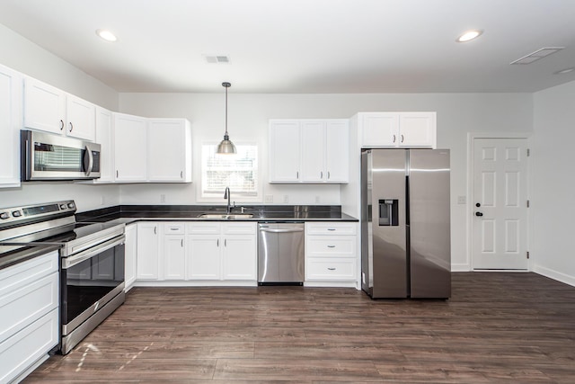 kitchen with stainless steel appliances, dark countertops, white cabinets, and decorative light fixtures