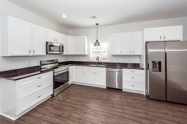 kitchen with stainless steel appliances, a sink, visible vents, hanging light fixtures, and dark countertops