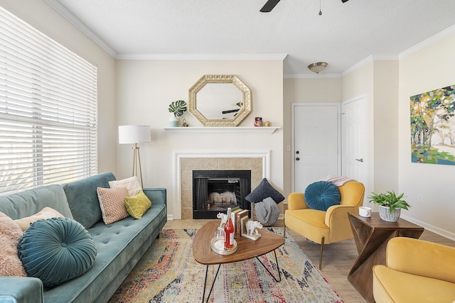 living room with a textured ceiling, ornamental molding, a tile fireplace, ceiling fan, and light hardwood / wood-style floors