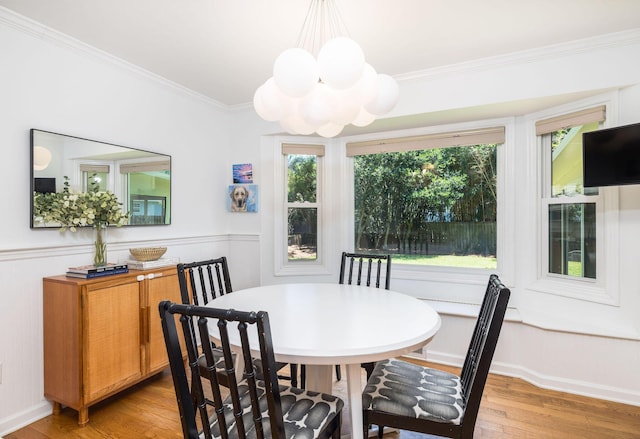 dining space featuring light wood-style floors, an inviting chandelier, crown molding, and wainscoting