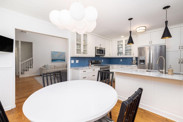 kitchen with stainless steel appliances, white cabinetry, glass insert cabinets, and light stone counters