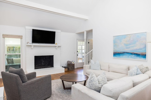 living area featuring vaulted ceiling with beams, a fireplace, stairway, and wood finished floors