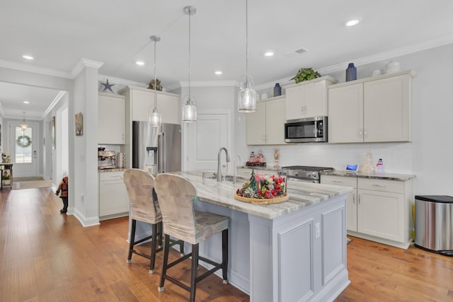 kitchen featuring sink, a kitchen island with sink, white cabinetry, high quality appliances, and decorative light fixtures