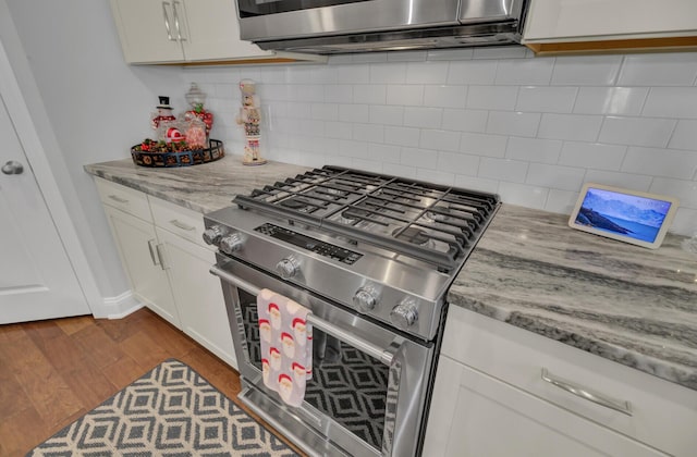 kitchen with stainless steel appliances, white cabinetry, light stone countertops, and dark hardwood / wood-style flooring