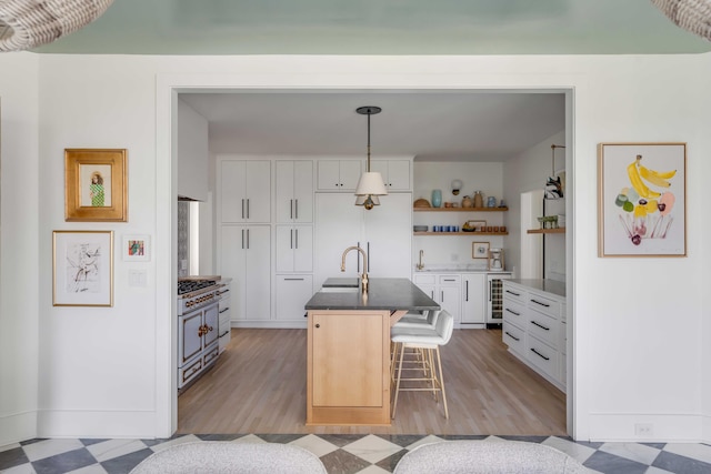 kitchen featuring white cabinets, gas range, pendant lighting, a center island with sink, and a breakfast bar