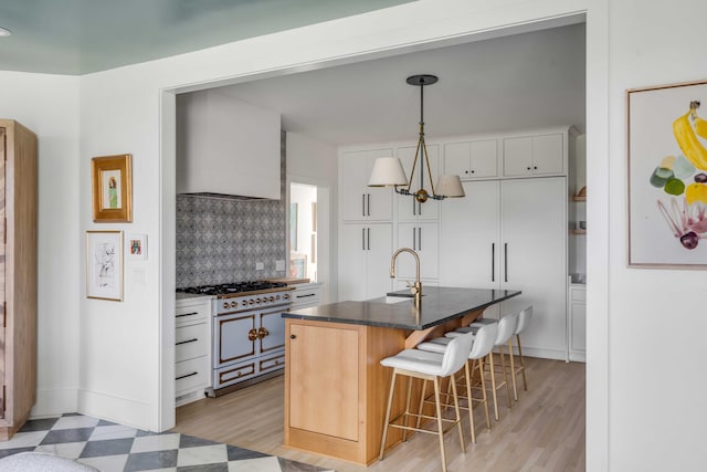 kitchen with a kitchen island with sink, white cabinetry, backsplash, decorative light fixtures, and a breakfast bar area