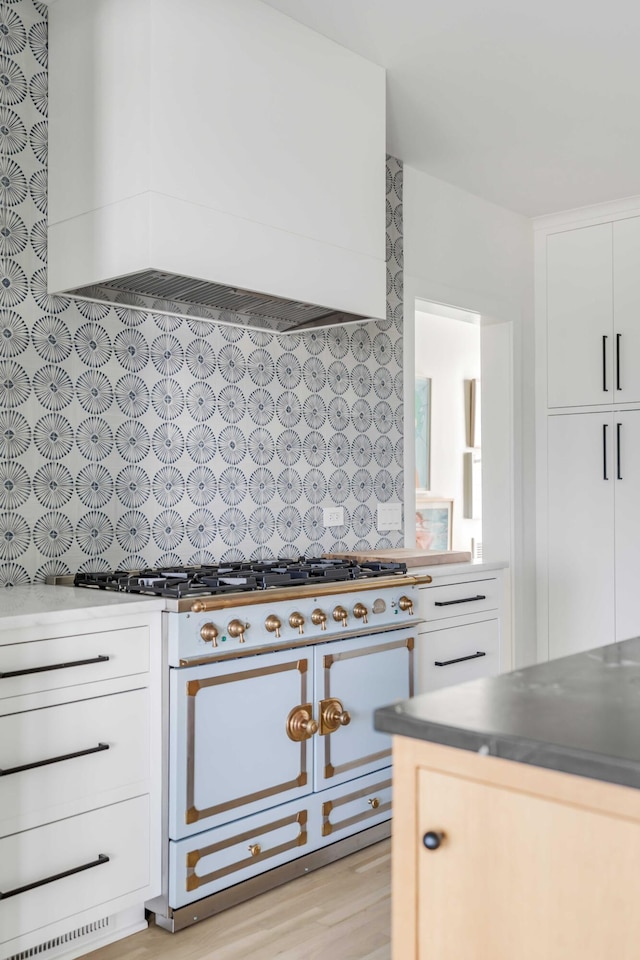 kitchen with backsplash, custom range hood, light hardwood / wood-style flooring, gas range, and white cabinetry