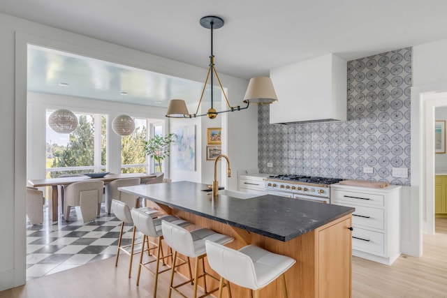 kitchen featuring white stove, white cabinetry, a kitchen bar, an island with sink, and sink