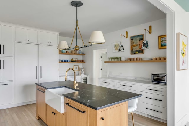 kitchen featuring light brown cabinetry, light hardwood / wood-style floors, an island with sink, sink, and white cabinets