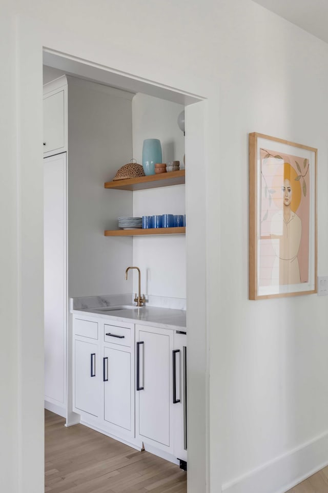 bar featuring sink, white cabinets, and light hardwood / wood-style floors