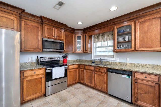 kitchen with a sink, light stone counters, brown cabinetry, and stainless steel appliances