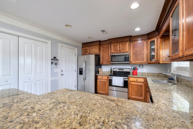 kitchen featuring ornamental molding, glass insert cabinets, brown cabinets, a sink, and stainless steel appliances