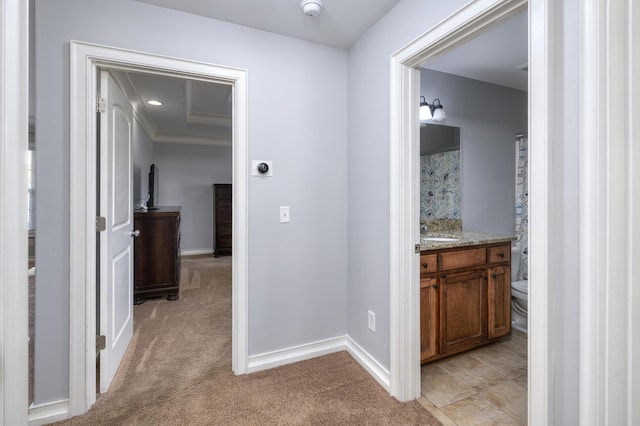 hall with crown molding, a sink, baseboards, and light carpet