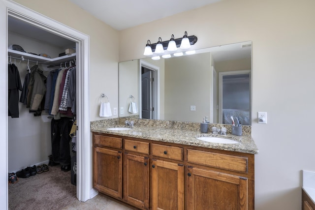 ensuite bathroom with double vanity, a walk in closet, and a sink
