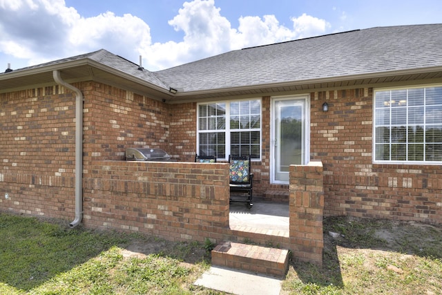 property entrance with brick siding, a shingled roof, a patio, and area for grilling