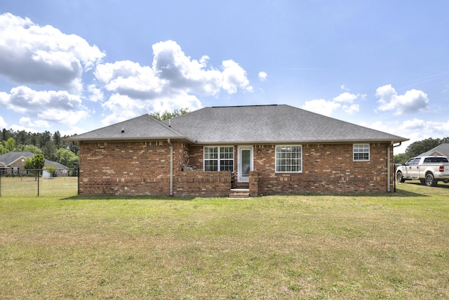 rear view of house with a lawn, fence, and brick siding