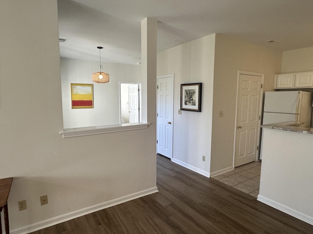 interior space featuring white refrigerator, wood-type flooring, hanging light fixtures, and white cabinets