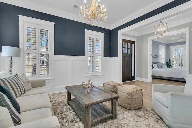 living area featuring wood finished floors, a decorative wall, wainscoting, crown molding, and a chandelier