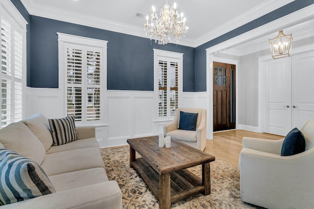 living area with a wainscoted wall, ornamental molding, an inviting chandelier, and wood finished floors