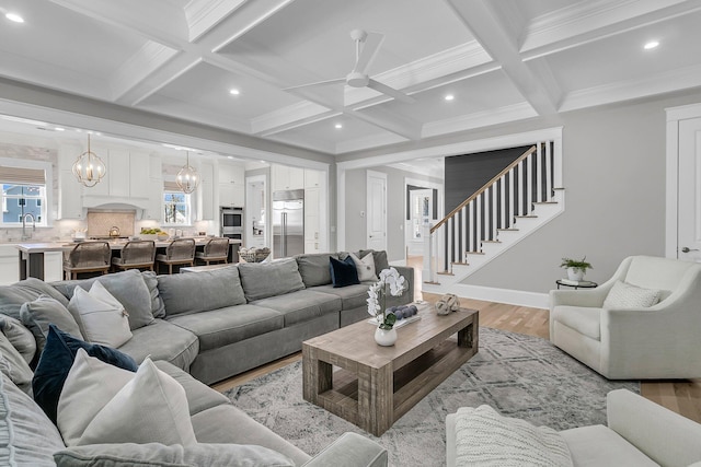 living area featuring stairway, baseboards, light wood-style floors, and beam ceiling