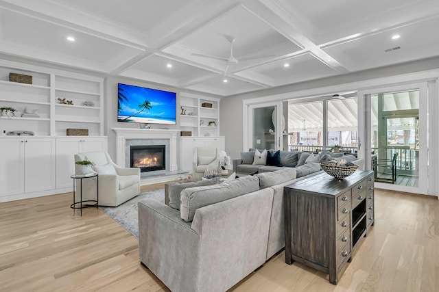 living area with beamed ceiling, built in features, light wood-style flooring, a glass covered fireplace, and coffered ceiling