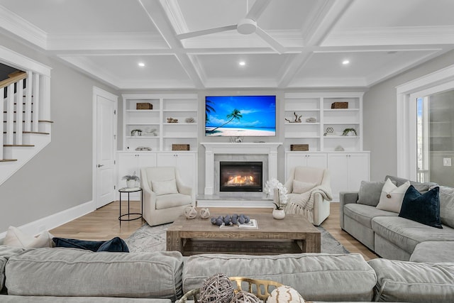 living room featuring a glass covered fireplace, light wood-style flooring, coffered ceiling, and beamed ceiling