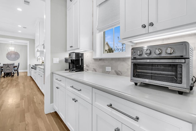 kitchen featuring decorative backsplash, white cabinets, visible vents, and light wood-style floors