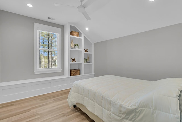 bedroom featuring light wood finished floors, visible vents, a wainscoted wall, vaulted ceiling, and a ceiling fan