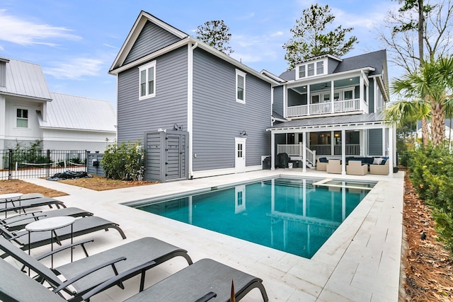 rear view of property featuring a pool with connected hot tub, fence, outdoor lounge area, a balcony, and a patio area