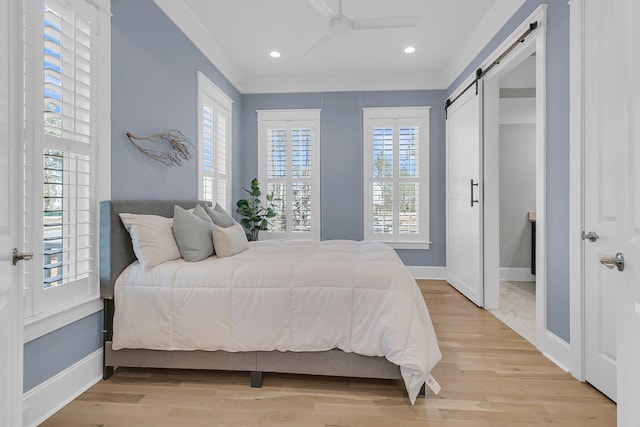 bedroom featuring a barn door, light wood-style floors, baseboards, and ornamental molding