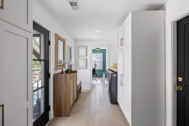 interior space with light wood-type flooring, washing machine and dryer, a healthy amount of sunlight, and visible vents