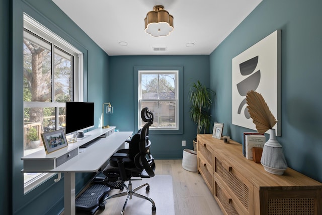 office space with light wood-style flooring, plenty of natural light, visible vents, and baseboards