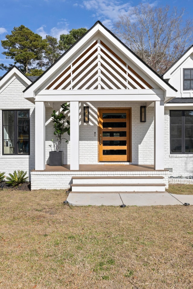 view of front of home featuring covered porch, a front lawn, and brick siding