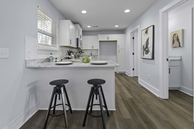 kitchen with a peninsula, a sink, white cabinetry, stainless steel microwave, and backsplash