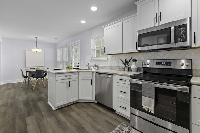 kitchen featuring tasteful backsplash, dark wood finished floors, appliances with stainless steel finishes, a peninsula, and white cabinets