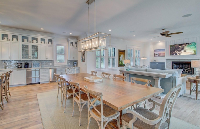 dining room with ceiling fan with notable chandelier, light wood-type flooring, a wealth of natural light, and a fireplace